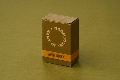 A compact, olive-green box labeled “Kent of Inglewood Potassium Alum Block” stands upright on a coordinating green surface, evoking the classic grooming benefits of potassium alum—a natural mineral often favored as a deodorant.