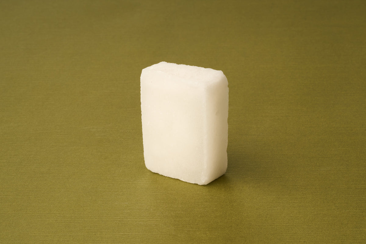 A single Kent of Inglewood Potassium Alum Block, rectangular and white, stands upright on a smooth olive green surface, resembling traditional alum blocks.