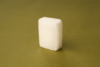 A single Kent of Inglewood Potassium Alum Block, rectangular and white, stands upright on a smooth olive green surface, resembling traditional alum blocks.