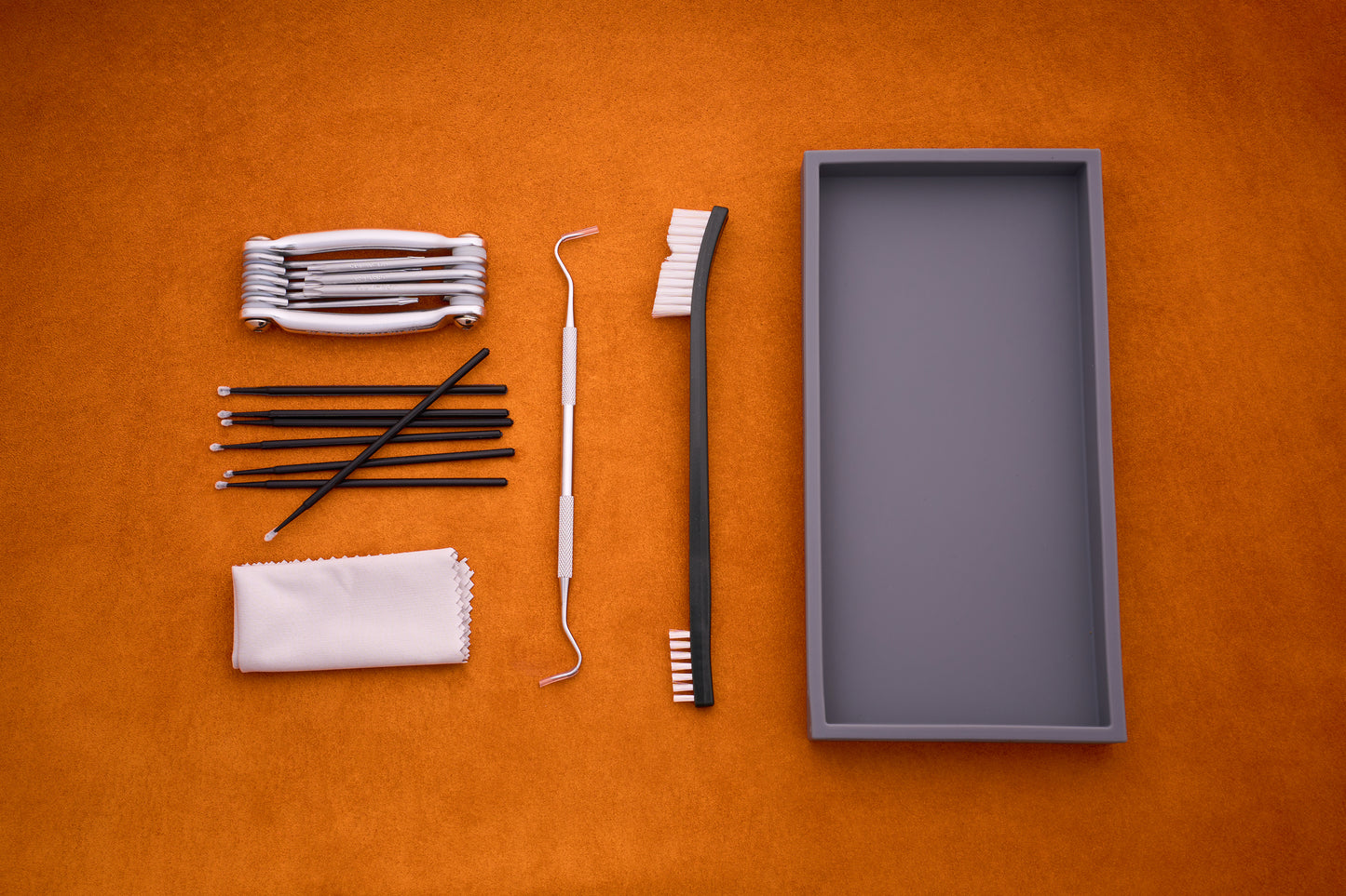 The Kent of Inglewood Pocket Knife Care Kit is displayed with its various tools—including a toothbrush, dental tools, detailing swabs, interdental brushes, a cloth, and a white retainer case—neatly arranged on an orange surface.