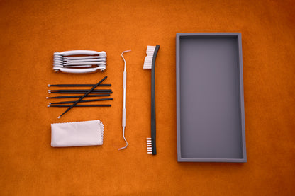 The Kent of Inglewood Pocket Knife Care Kit is displayed with its various tools—including a toothbrush, dental tools, detailing swabs, interdental brushes, a cloth, and a white retainer case—neatly arranged on an orange surface.