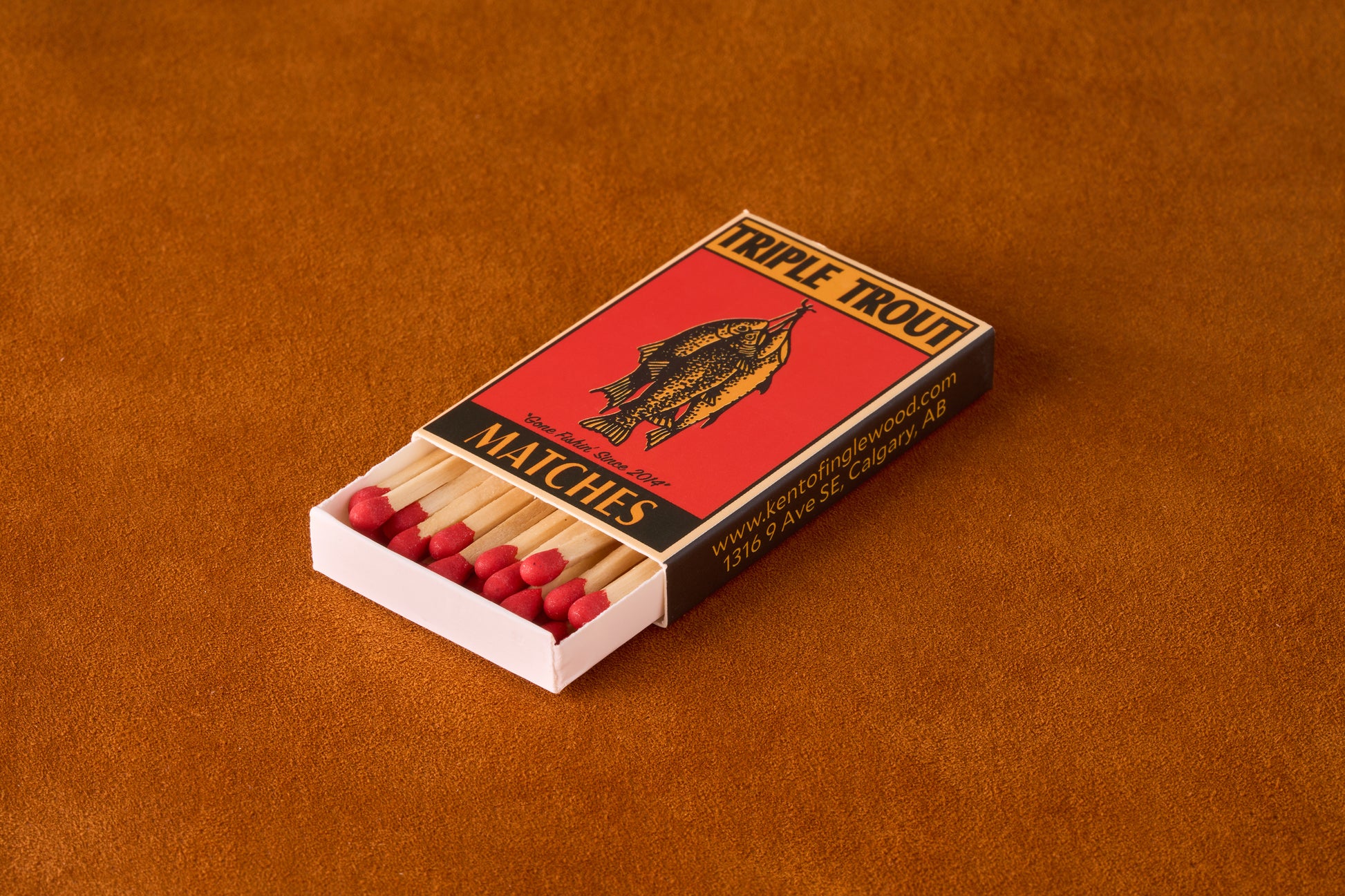Kent of Inglewood Trail Matches in a branded matchbox with three trout illustration, featuring durable wooden matches with red heads on a rust-orange surface.