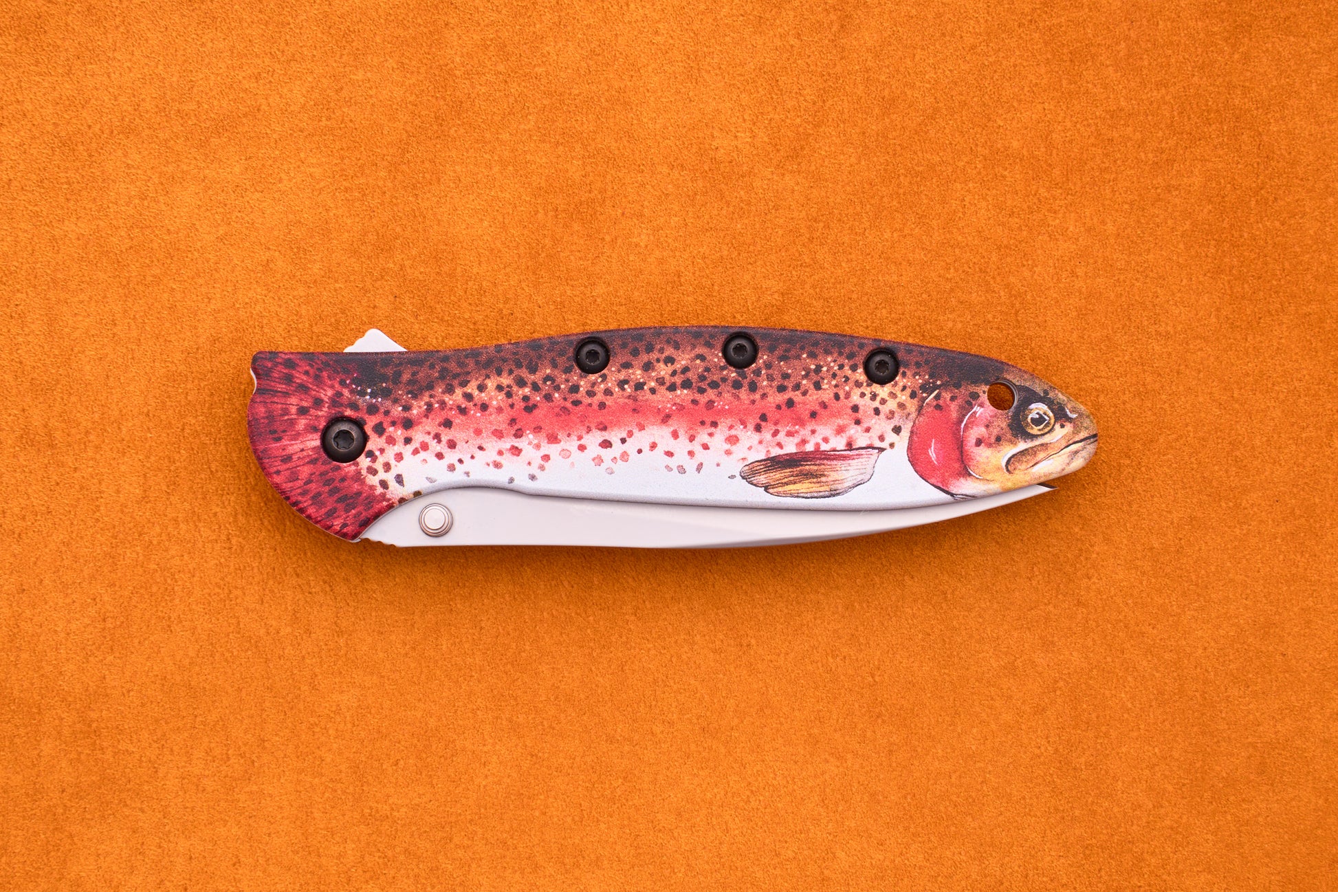 A Kershaw Leek Rainbow Trout folding pocket knife, featuring a handle designed to resemble a colorful fish, shown against an orange background.
