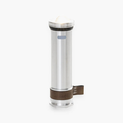 Barebones Mini Flashlight with ribbed metal body, glowing lens, leather wrist-strap, and magnetic base, ideal for versatile use in outdoor settings.