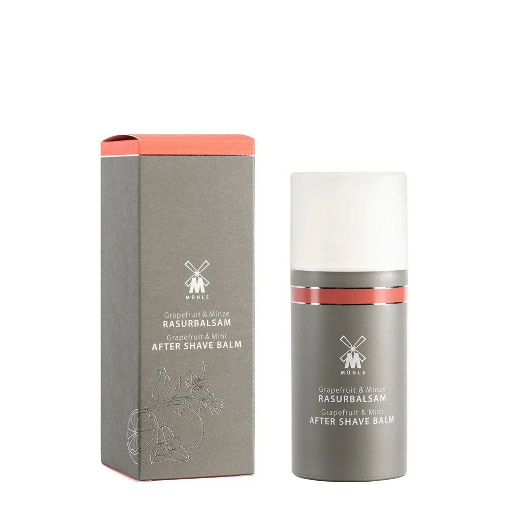 A bottle and box of Mühle Grapefruit & Mint Aftershave Balm, presented in minimalist grey packaging accented with red details and white lettering, featuring a subtle grapefruit illustration on the box. This natural aftershave balm offers an invigorating blend of grapefruit and mint for a refreshing, soothing post-shave experience.
