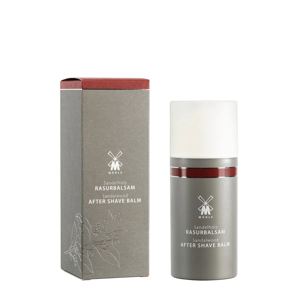 A bottle of Mühle Sandalwood Aftershave Balm is placed beside its coordinating gray box, both adorned with crisp white text and minimalist design. This gentle aftershave balm from Mühle provides ideal post-shave care, combining soothing nourishment with a warm sandalwood fragrance for refreshed skin.