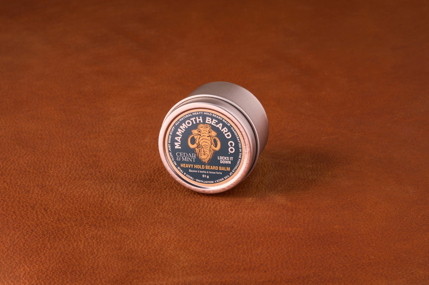 Mammoth Beard Co. Beard Balm Cedar and Mint 60ml tin on leather surface, featuring a mammoth logo and Locks It Down label, ideal for moisturizing and taming beards.
