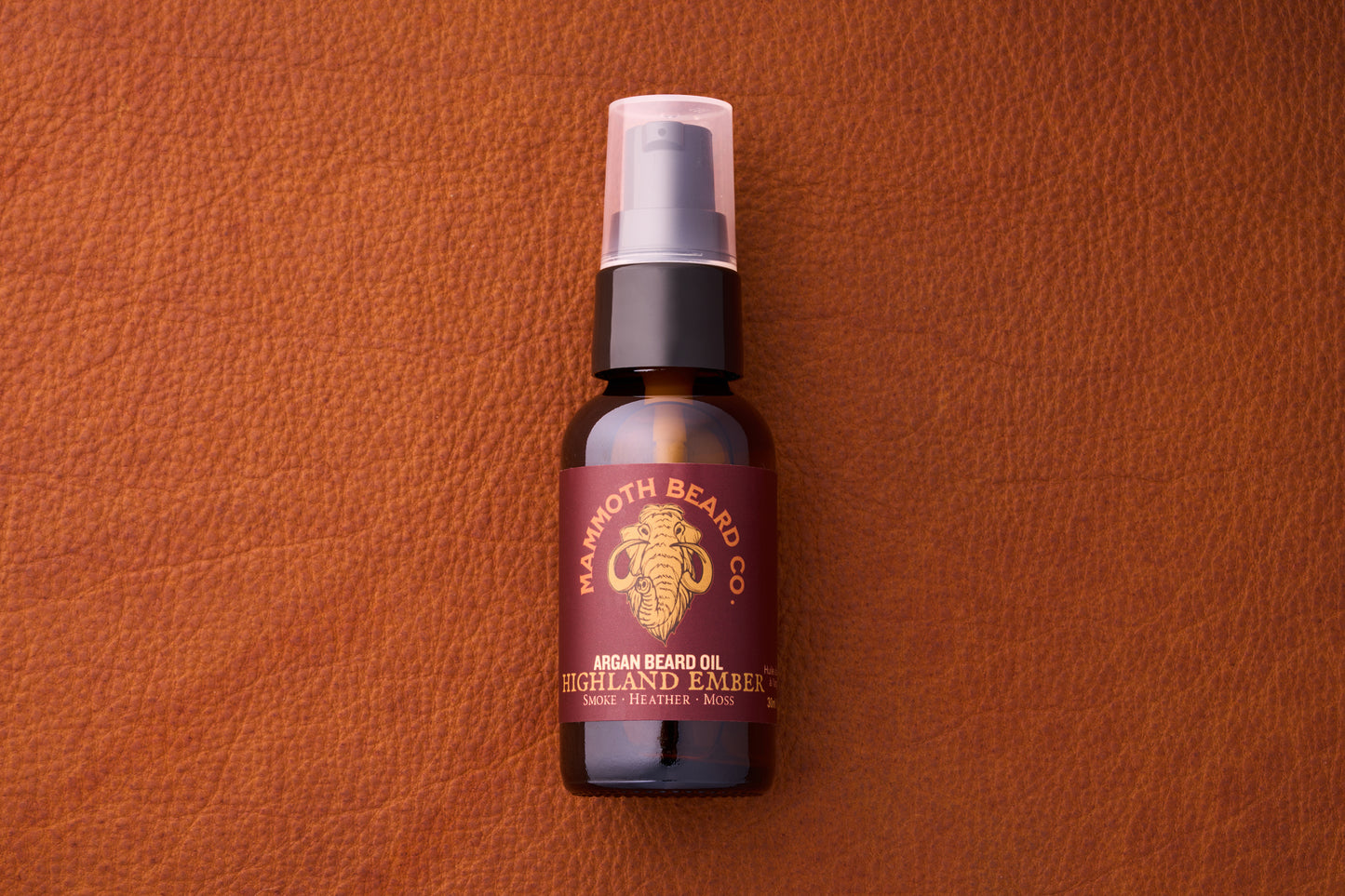 Mammoth Beard Co. Argan Beard Oil - Highland Ember, 30ml amber bottle with pump, on leather; noted for smoky, heather, and moss scent notes.