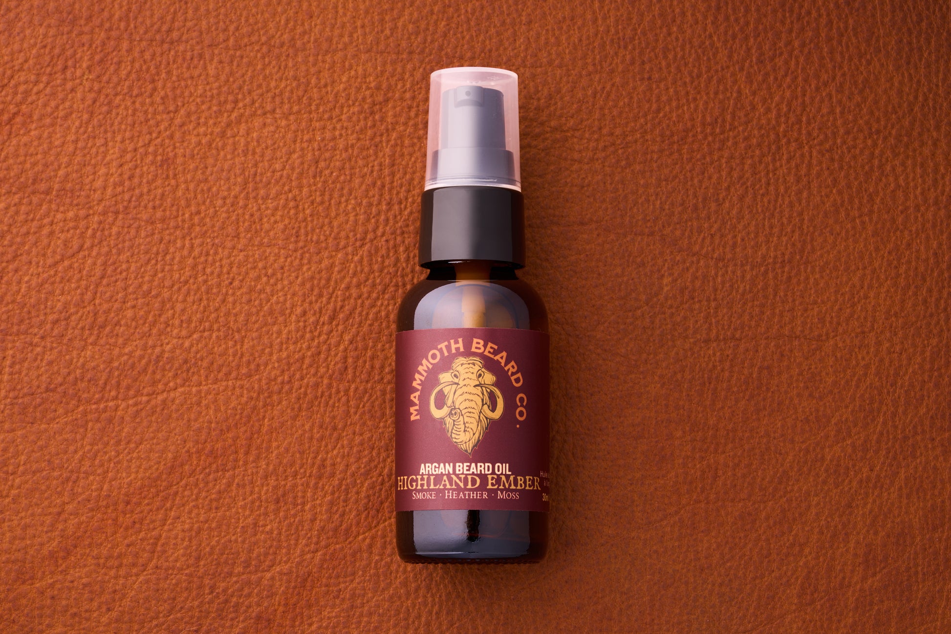 Mammoth Beard Co. Argan Beard Oil - Highland Ember, 30ml amber bottle with pump, on leather; noted for smoky, heather, and moss scent notes.