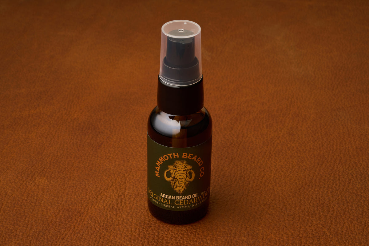 A bottle of Mammoth Beard Co. Beard Oil - Original Cedarwood 30ml with a spray cap rests on a textured brown leather surface, highlighting the premium quality of natural ingredients found in all their beard care products.