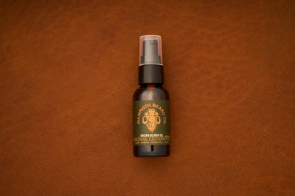 A small dark brown bottle of Mammoth Beard Co. Beard Oil - Original Cedarwood 30ml, expertly crafted with natural ingredients, sits with a spray cap on a textured brown leather surface.