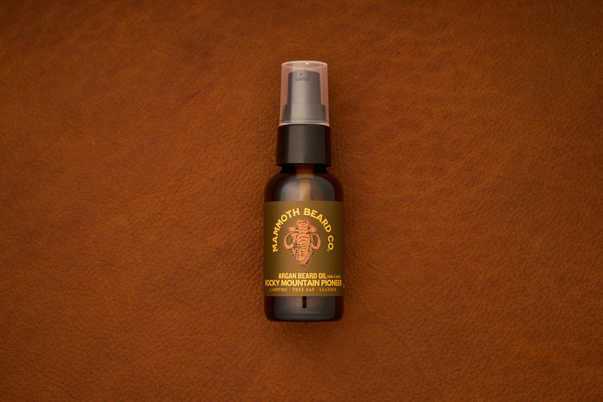 A brown bottle of Mammoth Beard Co. Beard Oil - Rocky Mountain Pioneer 30ml, crafted with natural ingredients, rests on a textured brown leather surface—an essential choice for those seeking premium beard care products.