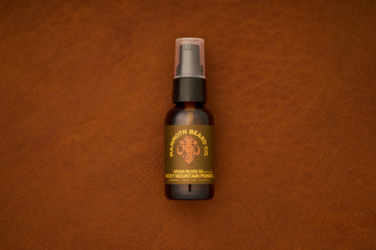 A brown bottle of Mammoth Beard Co. Beard Oil - Rocky Mountain Pioneer 30ml, crafted with natural ingredients, rests on a textured brown leather surface—an essential choice for those seeking premium beard care products.