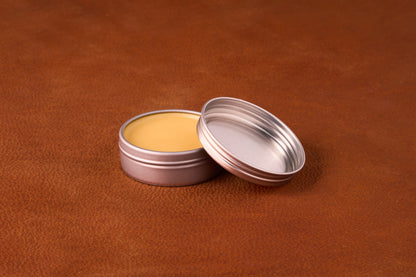 Mammoth Beard Co. Sex & Cigars Moustache Wax 1oz, in an open tin, displayed on a leather surface, highlighting its smooth texture ideal for versatile styling.