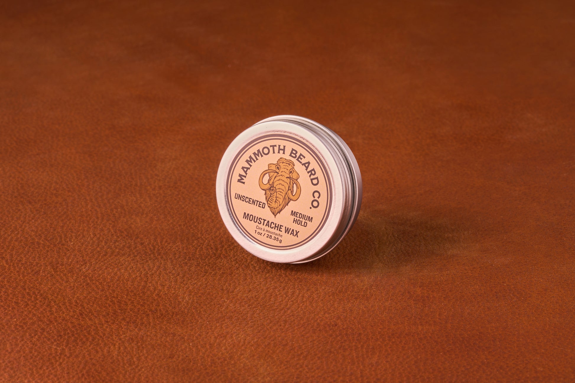 Mammoth Beard Co. Unscented Moustache Wax tin on leather surface, offering medium hold for versatile styling, ideal for casual looks and easy portability.
