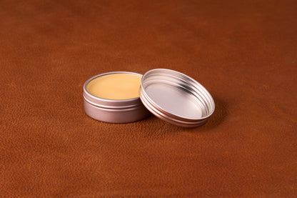 Mammoth Beard Co. Unscented Moustache Wax in an open metal tin showcasing smooth, pale yellow balm on a brown textured surface, ideal for versatile styling.