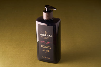 A pump bottle of Mistral Body Lotion - Bourbon Vanilla rests on an olive-green surface. The 15.5 fl oz (460 ml) bottle displays gold and white text on the label, emphasizing its French fragrance.
