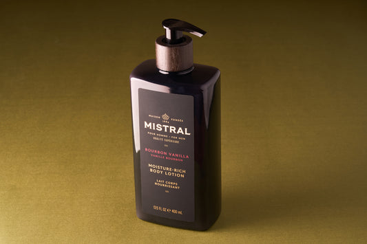 A pump bottle of Mistral Body Lotion - Bourbon Vanilla rests on an olive-green surface. The 15.5 fl oz (460 ml) bottle displays gold and white text on the label, emphasizing its French fragrance.