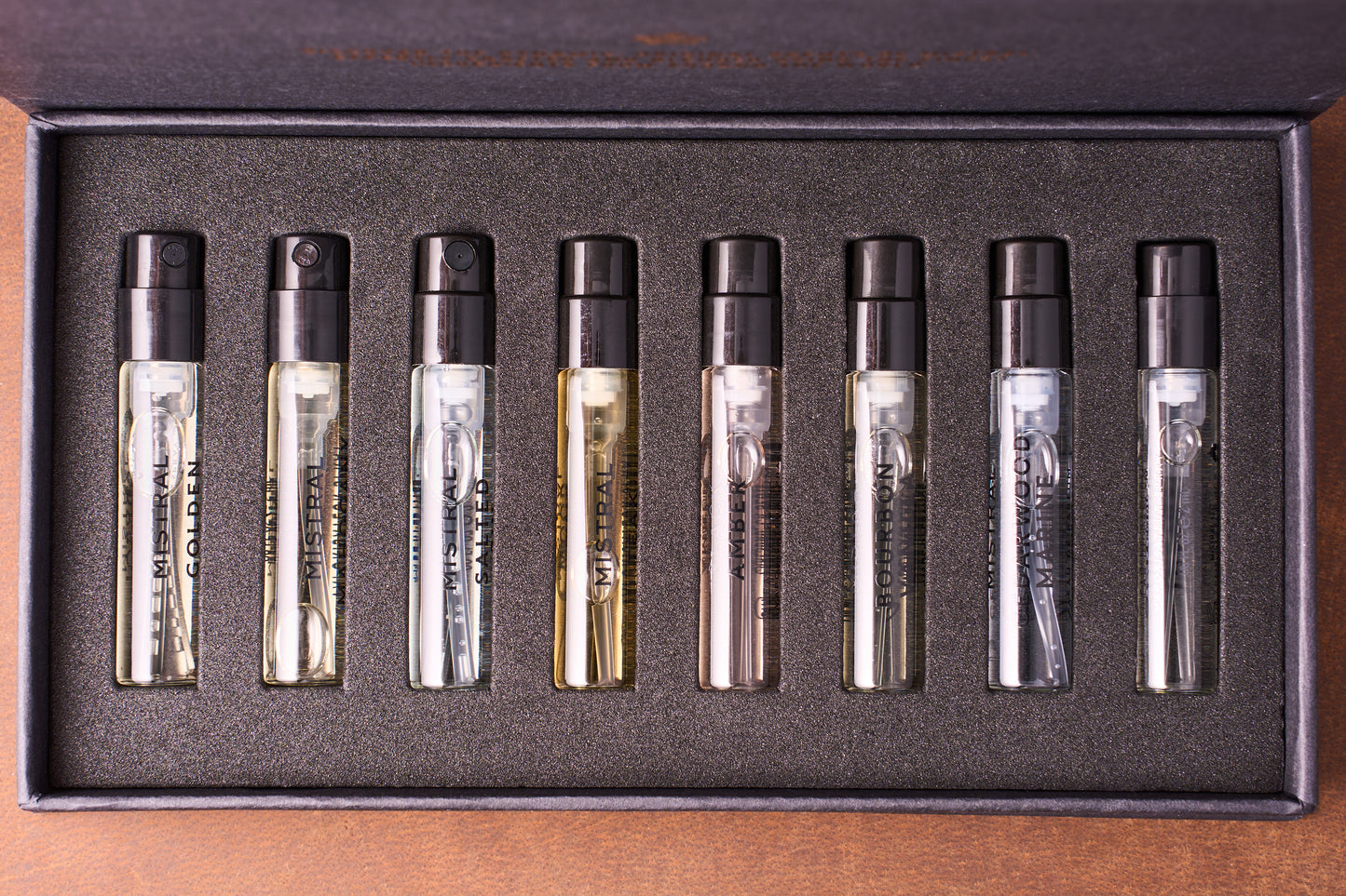 The Mistral Eau de Parfum Discovery Set includes eight labeled sample vials with black spray tops, each containing a unique French men's fragrance, arranged in a sleek, foam-lined box.