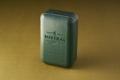 A rectangular, dark green Mistral For Men Cypress Oak Bar Soap stands upright on a gold surface, featuring embossed French text and sharp edges that highlight its refined craftsmanship and masculine elegance.
