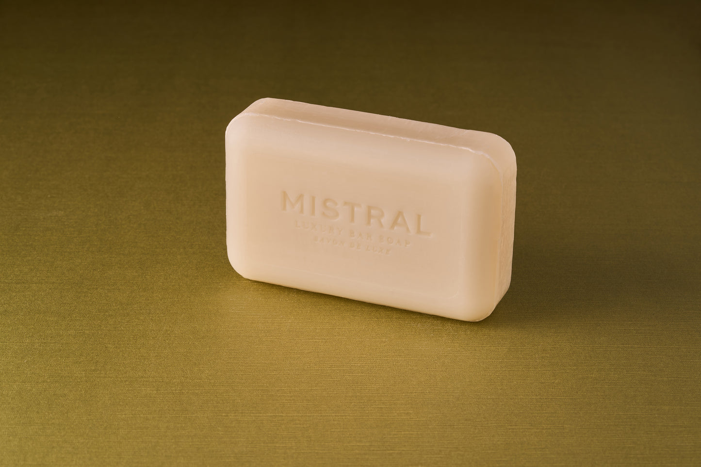 A rectangular beige bar of Mistral Marbles Dahlia Bar Soap rests on a textured olive-green surface.