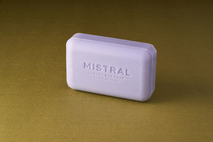 The Mistral Marbles Lavender Bar Soap, a rectangular bar embossed with its name, rests on a golden-brown textured surface, radiating timeless elegance and classic French lavender fragrance.