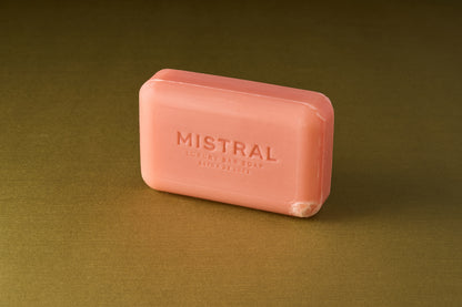 A pink rectangular bar of Mistral Marbles Lychee Rose Bar Soap, a triple-milled soap with a rich French fragrance, rests on a goldish-brown surface.