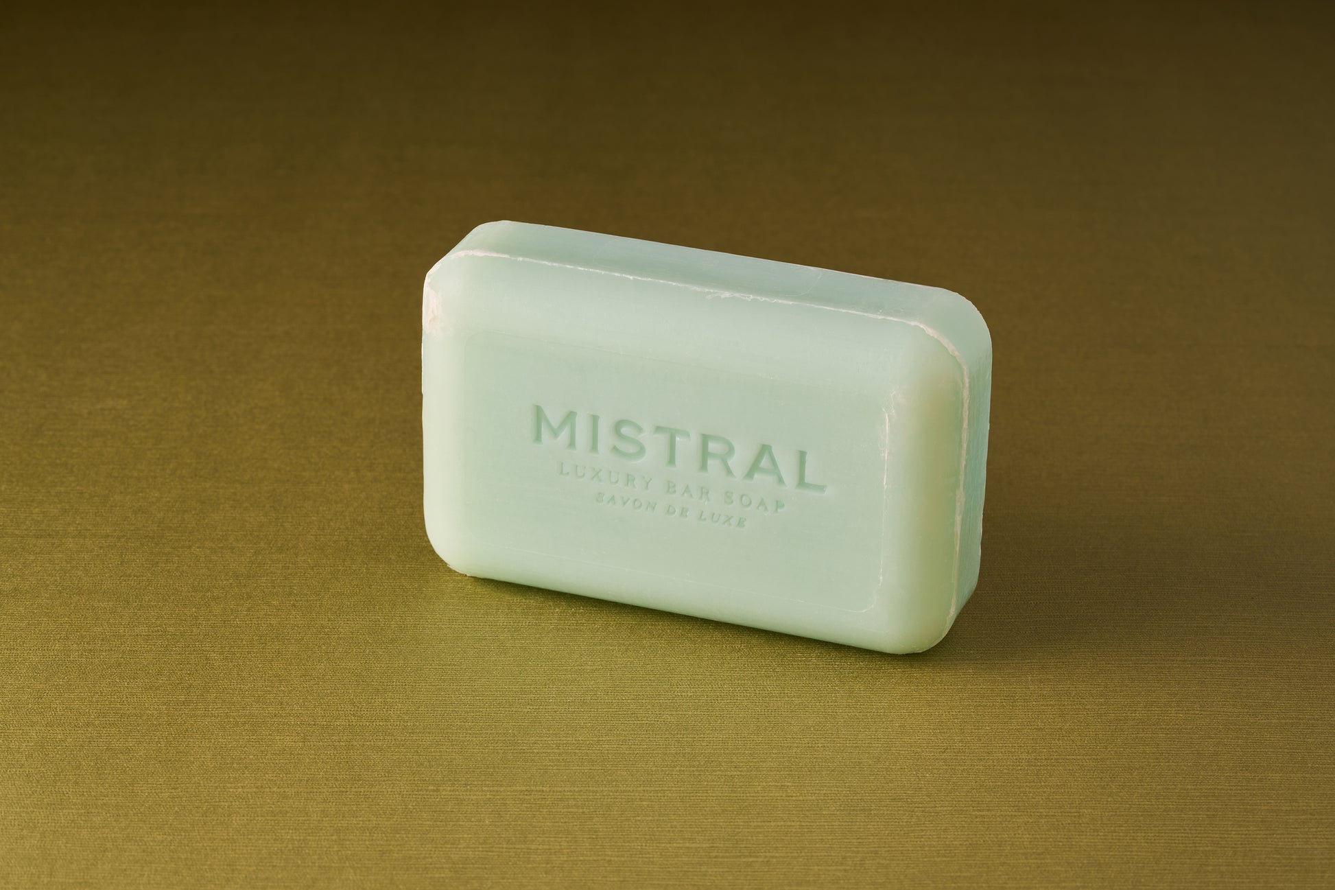 A rectangular, light green Mistral Marbles Marine Bar Soap rests on a plain olive surface, exuding a refined French-inspired fragrance.