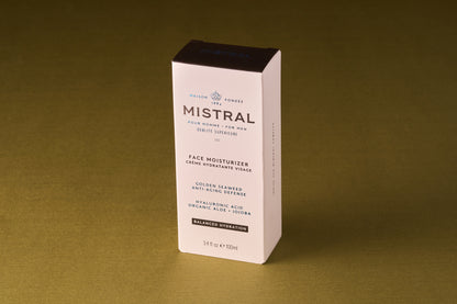 A box of Mistral Performance Series Face Moisturizer rests on a gold surface, its white packaging with black text showcasing golden seaweed, hyaluronic acid, and aloe—capturing the sophistication of a French fragrance.
