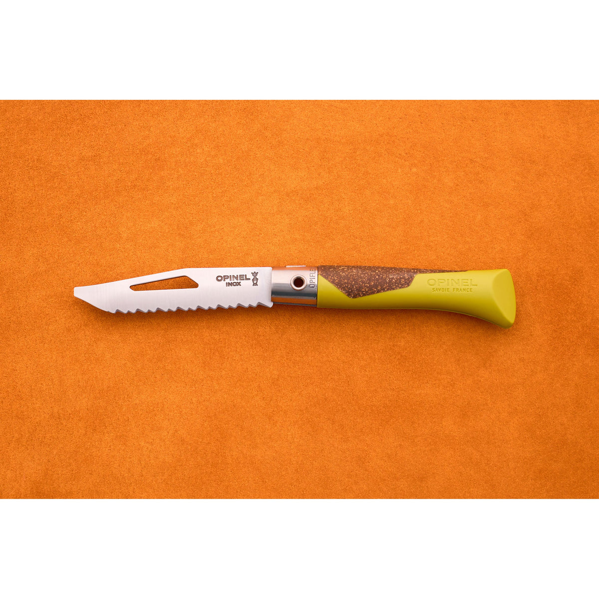 An Opinel Neo 7 Alpine kitchen knife with a green and wood handle is placed on an orange textured surface. The serrated blade, inspired by the classic Opinel pocket knife design, features a slot near the tip and displays the Opinel branding.