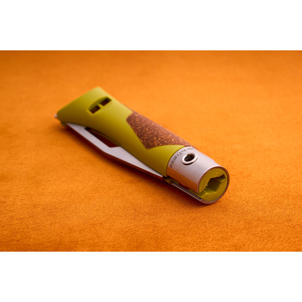 A close-up of the Opinel Neo 7 Alpine, a green and brown utility knife with a retractable blade designed as a versatile mountain tool, placed on an orange textured surface.