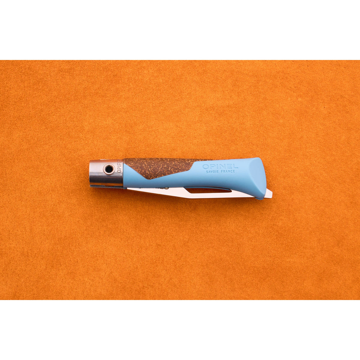 A blue and brown Opinel Neo 7 Alpine pocket knife is closed and placed on an orange surface, displaying the handle with the brand name and a partially visible locking ring—an essential mountain tool for any adventure.