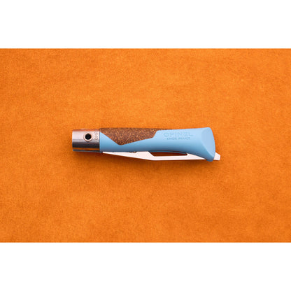 A blue and brown Opinel Neo 7 Alpine pocket knife is closed and placed on an orange surface, displaying the handle with the brand name and a partially visible locking ring—an essential mountain tool for any adventure.