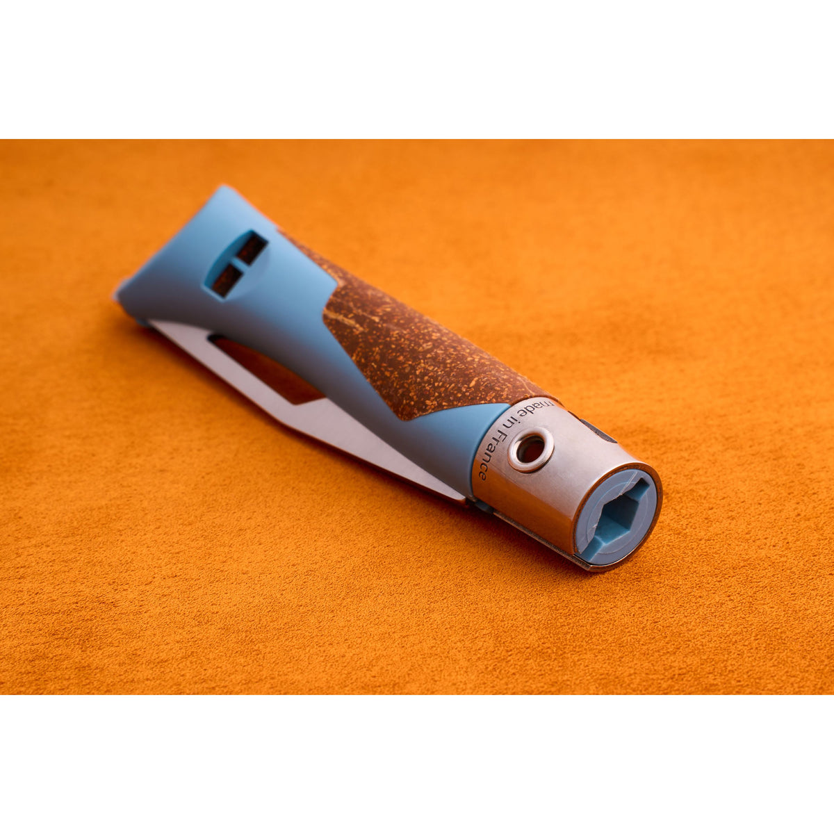 A blue and brown textured grip Opinel Neo 7 Alpine handle with a metal end rests on an orange surface. Reminiscent of a mountain tool, the handle features a hexagonal opening and engraved text near the metal part.
