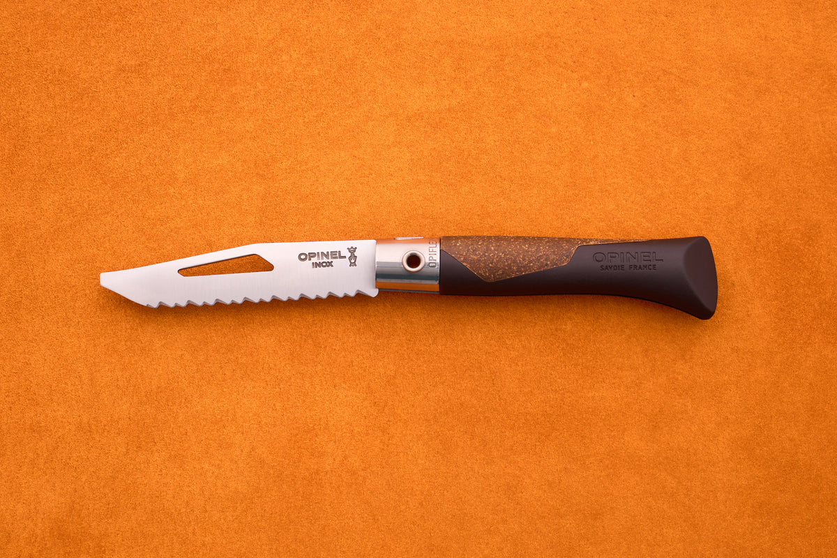 An Opinel Neo 7 Alpine pocket knife, featuring a serrated blade with a slot and a brown handle, rests on an orange textured surface.