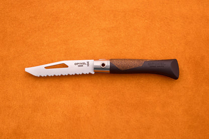 An Opinel Neo 7 Alpine pocket knife, featuring a serrated blade with a slot and a brown handle, rests on an orange textured surface.