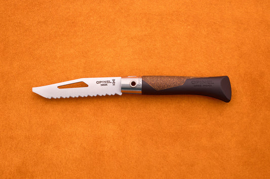 An Opinel Neo 7 Alpine pocket knife, featuring a serrated blade with a slot and a brown handle, rests on an orange textured surface.