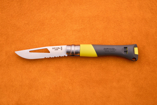 An Opinel No. 9 Ocean folding knife, featuring a partially serrated blade and a gray-yellow handle styled for sailing, is displayed on an orange surface.