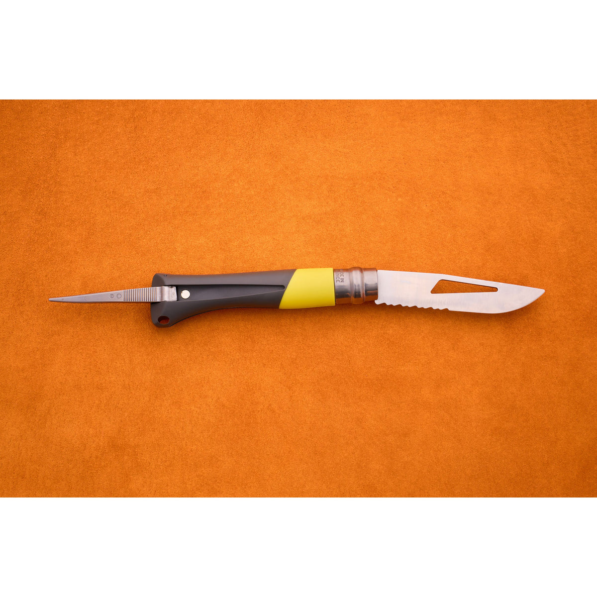 An Opinel No. 9 Ocean folding sailing knife with a black and yellow handle and a partially serrated blade lies open on an orange surface.