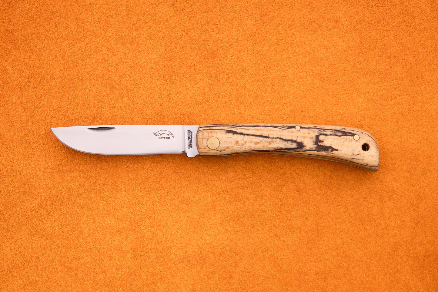 An Otter-Messer Hippe-Kniep, featuring a polished steel blade and a light wooden handle, rests on an orange textured surface, embodying the classic style of a traditional German farmers knife.