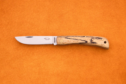An Otter-Messer Hippe-Kniep, featuring a polished steel blade and a light wooden handle, rests on an orange textured surface, embodying the classic style of a traditional German farmers knife.