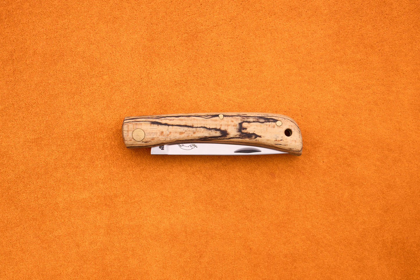 An Otter-Messer Hippe-Kniep folding pocket knife, featuring a wood-patterned handle and a partially visible blade reminiscent of a traditional farmer’s knife, is placed on an orange textured surface.