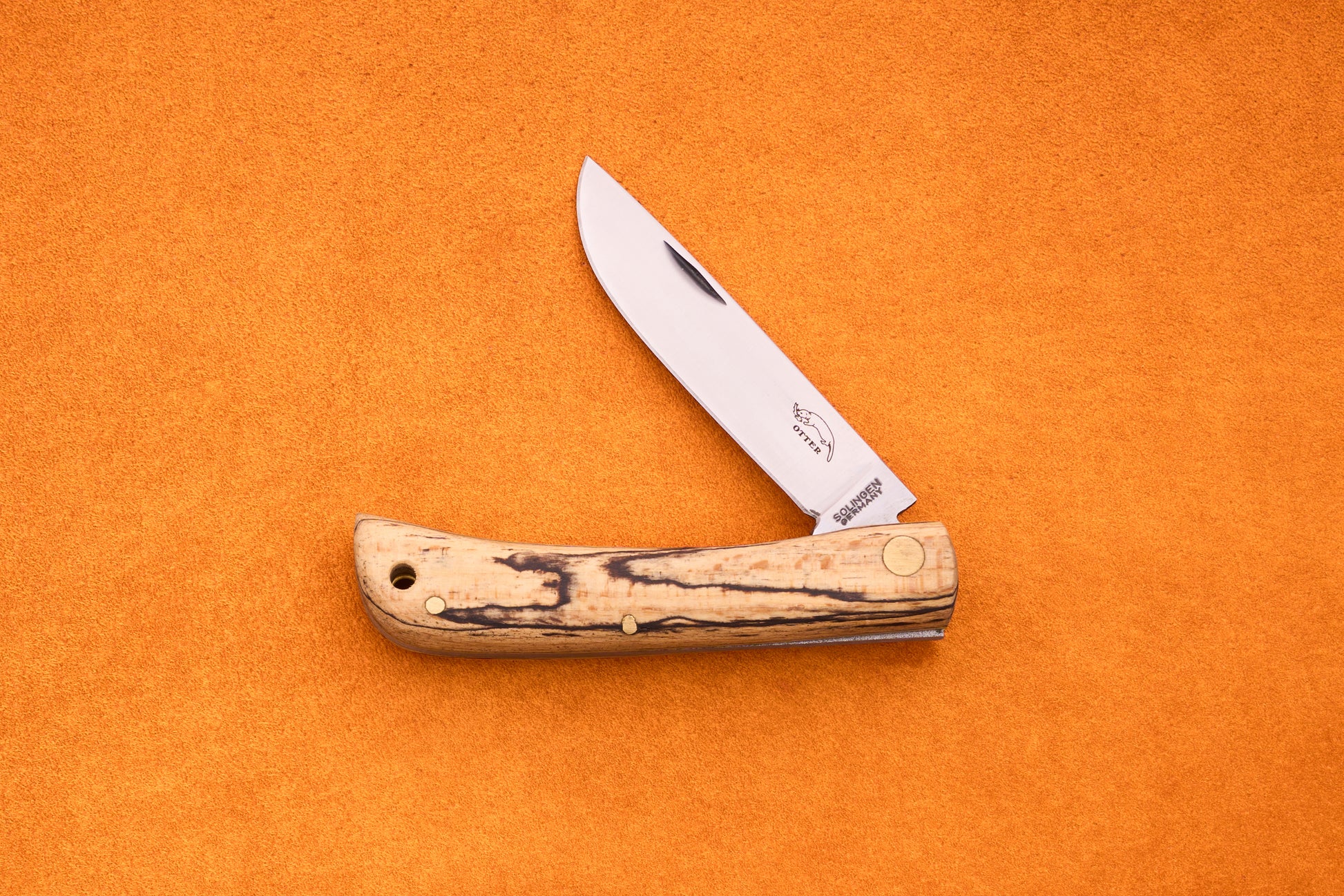 An Otter-Messer Hippe-Kniep, a handmade German knife featuring a wooden handle and a partially open silver blade, rests on an orange textured surface, evoking its heritage as a classic traditional farmer’s knife.