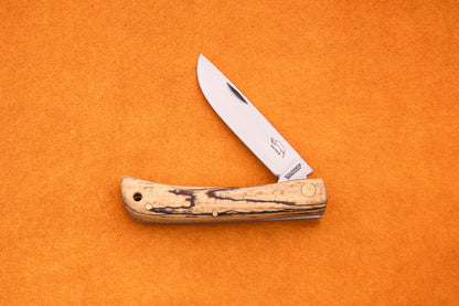 An Otter-Messer Hippe-Kniep, a handmade German knife featuring a wooden handle and a partially open silver blade, rests on an orange textured surface, evoking its heritage as a classic traditional farmer’s knife.