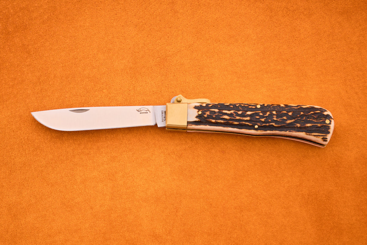 An Otter-Messer Hunting Pocket Knife with a partially open stainless steel blade and a textured brown and tan stag horn handle, resting on an orange surface.