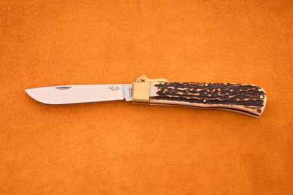 An Otter-Messer Hunting Pocket Knife with a partially open stainless steel blade and a textured brown and tan stag horn handle, resting on an orange surface.