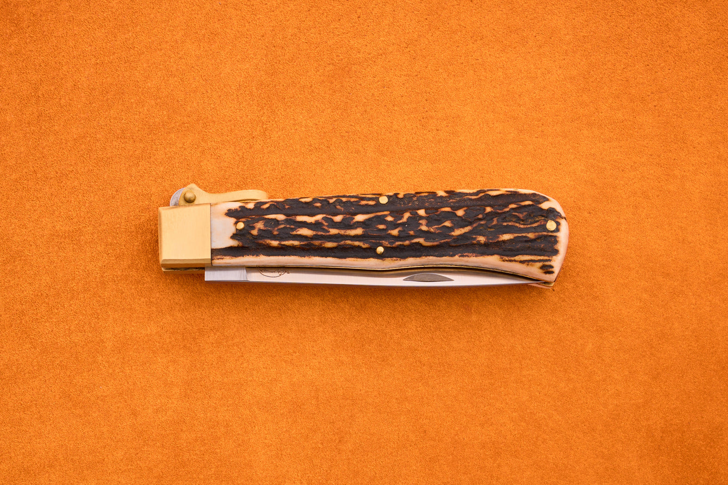 The Otter-Messer Hunting Pocket Knife, shown closed with a textured dark brown stag horn handle and brass bolster, is displayed on a bright orange background.