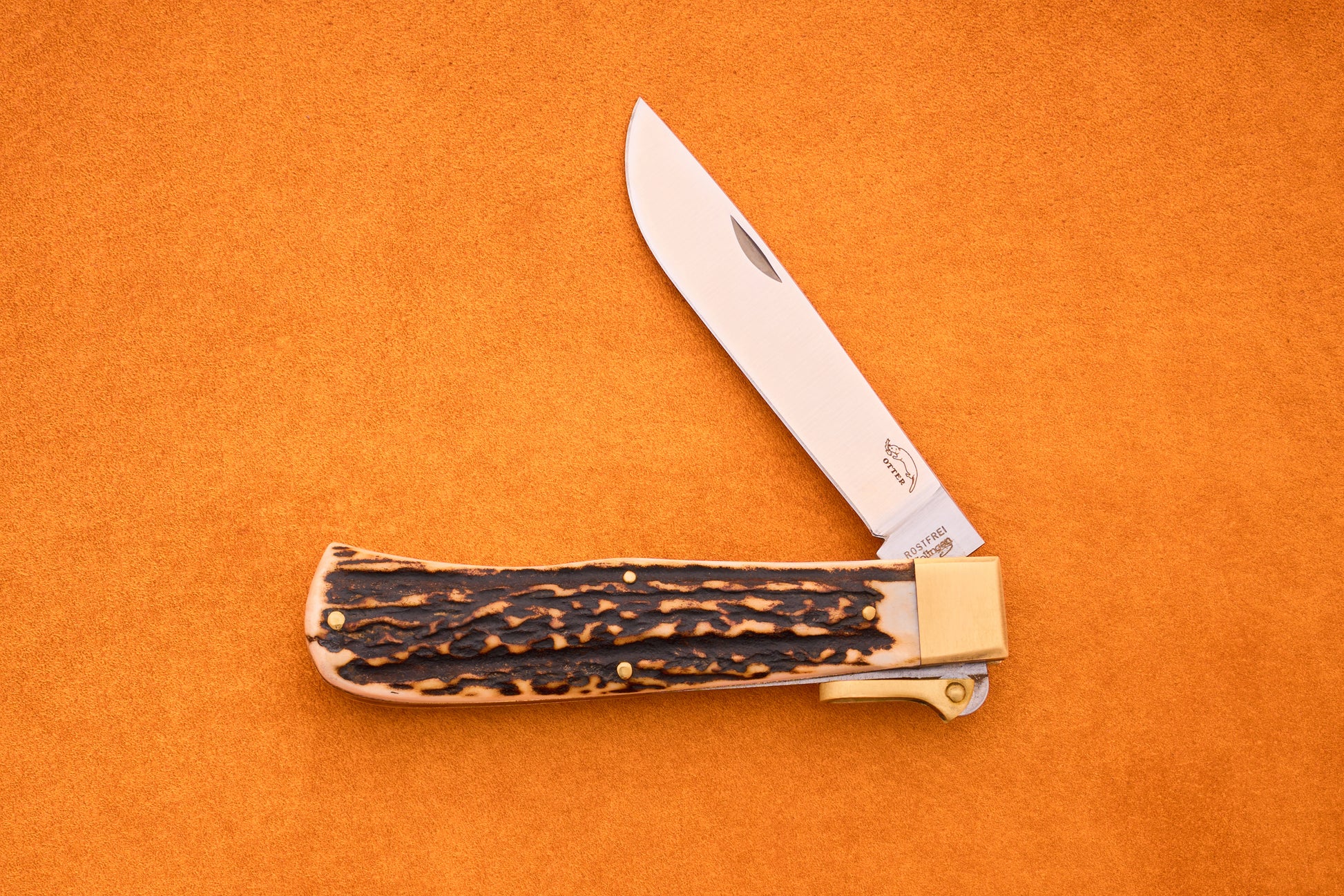 The Otter-Messer Hunting Pocket Knife, featuring a stag horn handle and a partially open silver blade, is displayed on an orange background.