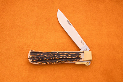 The Otter-Messer Hunting Pocket Knife, featuring a stag horn handle and a partially open silver blade, is displayed on an orange background.