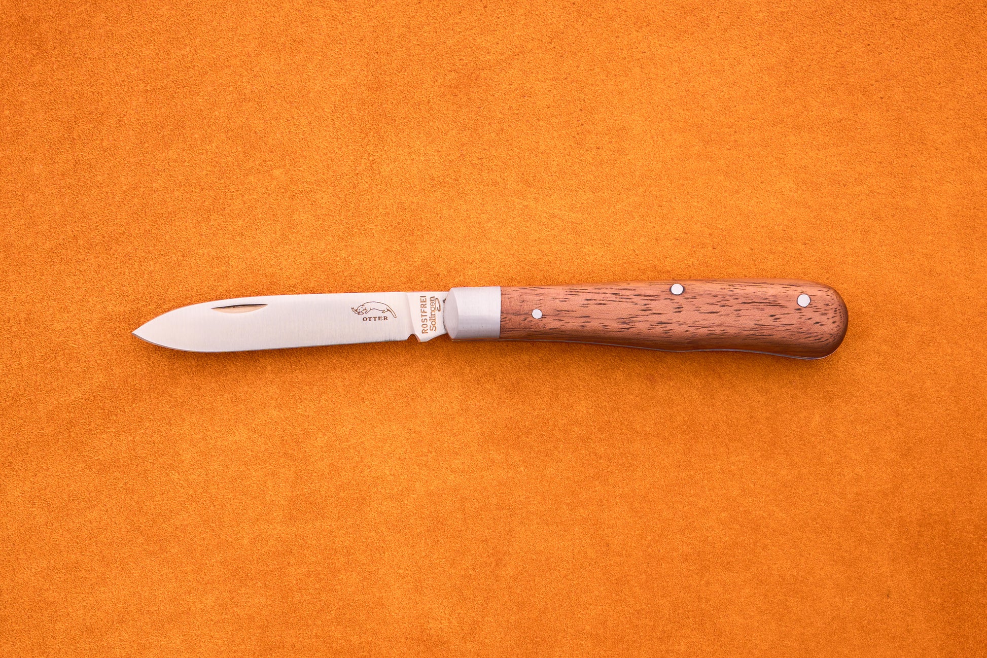 An Otter-Messer Pocket Knife Classic with a sapele wood handle and stainless steel blade lies closed on an orange textured surface.